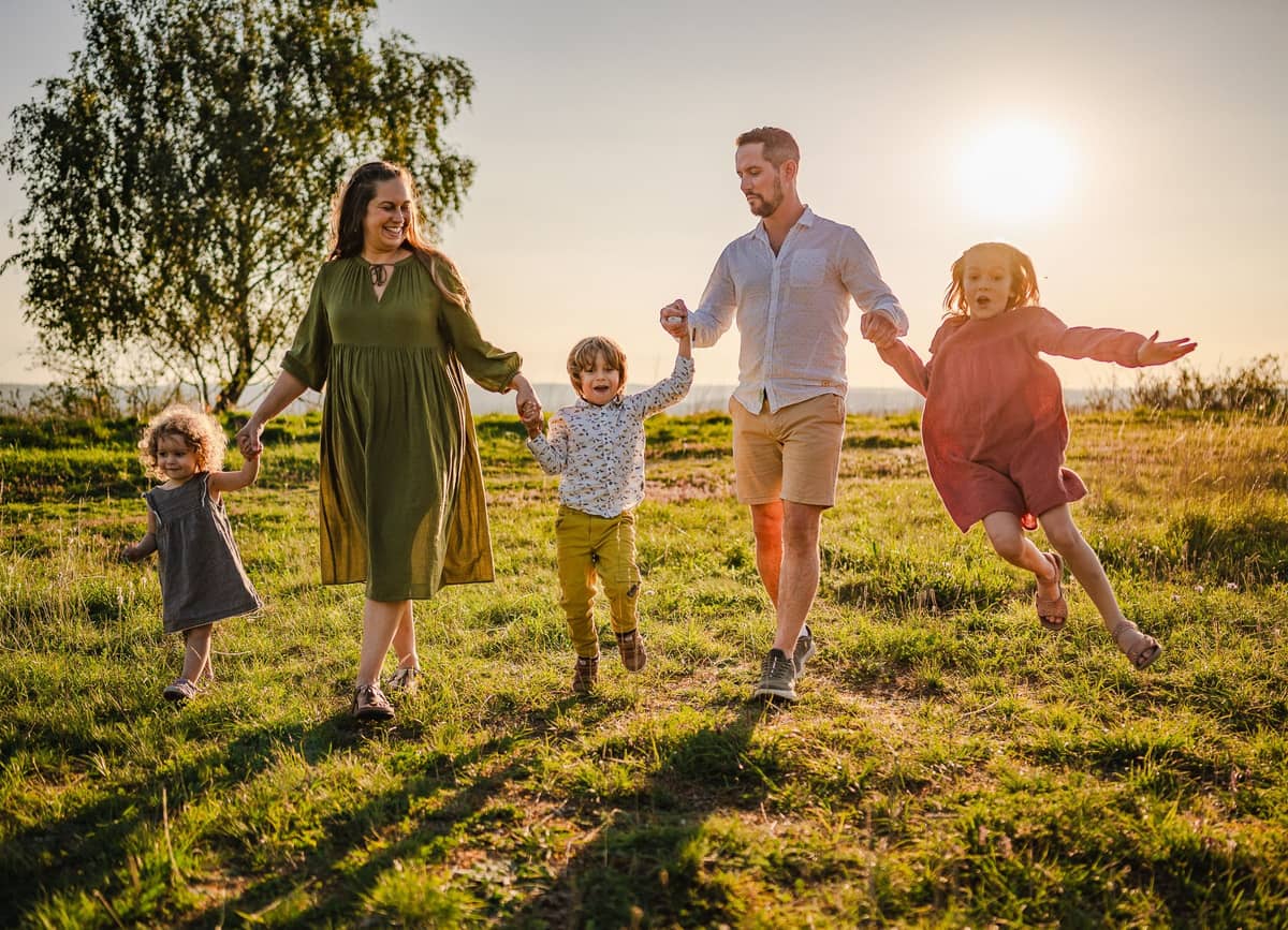 Familie läuft Hand in Hand über eine Wiese bei Sonnenuntergang